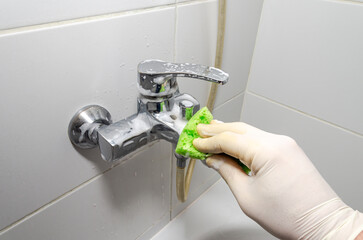 Housekeeper cleaning bathroom faucet with lime scale cleaner