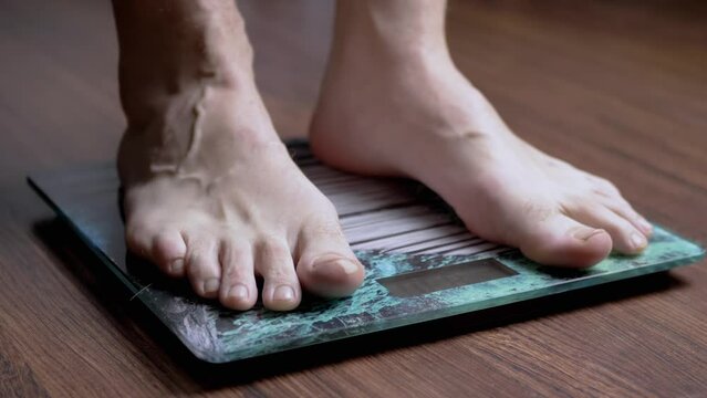 Male on the Scales Measures the Weight. Close up. A man barefoot steps on a transparent glass scale on the floor in the room. Step. Barefoot. Overweight, obesity. Control, weight check. Weightloss.