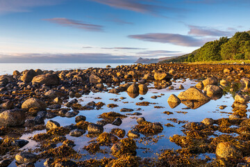 The rocky coastline at Corrie, Isle of Arran, Scotland, with the peak of Holy Island in the...