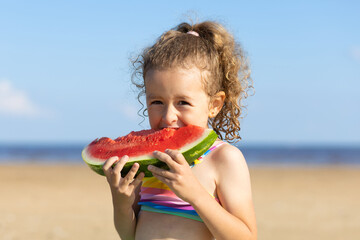 cute little girl eats ripe juicy red watermelon on the beach, coast, seashore. the concept of summer kid holidays, seasonal fruits and berries
