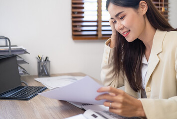 Portrait of happy businesswoman analyzing documents in office. Asian businesswoman sitting at desk reading documents. analyzing graph working on company project. © Fahng