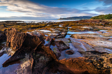 Sandstone patterns and finned bedrock along the rocky coastline at Pirate's Cove near Corrie, Isle of Arran, Scotland, with the peak of Holy Island in the distance.