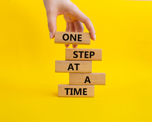 One step at a time symbol. Concept words One step at a time on wooden blocks. Beautiful yellow background. Businessman hand. Business and One step at a time concept. Copy space.