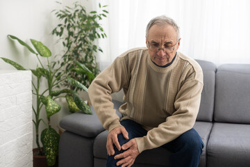 Fototapeta premium Knee pain in an elderly man. An old man holding his hand clutching his knee. Massage your foot.