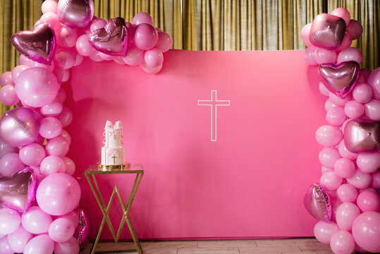 a large cake decorated with a bow on the background of a pink photo zone, which is decorated with pink and red balloons and hearts. festive photo zone for a girl for christening.