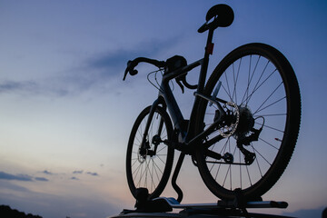 A sports bike is fixed on the roof of a car. Background of the evening sky.