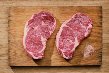 Two slices of raw beef fillet steaks on wooden board, top view. 