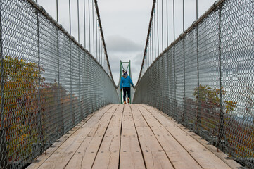 A low angle of a young woman walking down a suspension bridge over a valley during fall