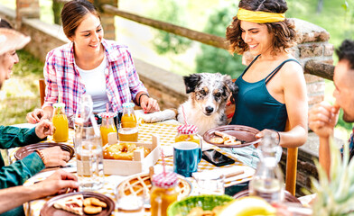 Young friends on healthy pic nic break fast with cute puppy at countryside farm house - Unplug life style concept with happy people having fun together out side at garden picnic party - Focus on dog - 584755692
