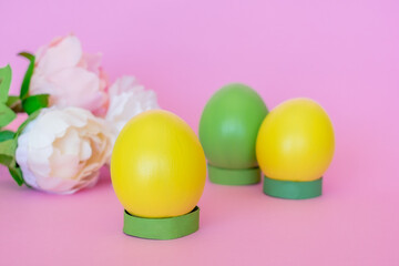 Easter eggs upright in yellow and green on a pink background along with flowers.