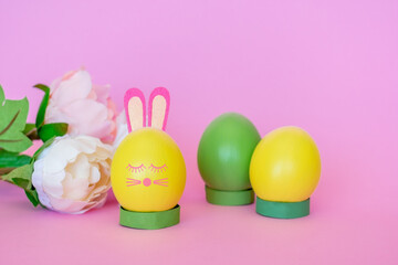 Easter eggs of yellow and green color with a decor in the form of a rabbit on a pink background.