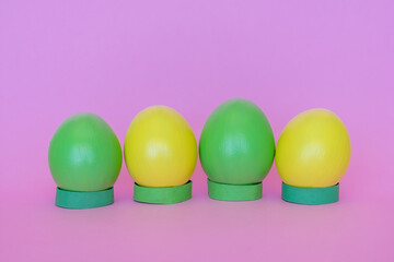 Easter eggs in a vertical position of yellow and green on a pink background.