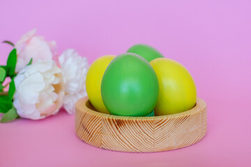 Obraz na płótnie Canvas Easter eggs in yellow and green color in a wooden plate on a pink background.
