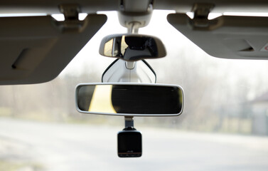 Helpful equipment. The close up of a black-rimmed rear-view mirror being adjusted to the clean windshield of a car