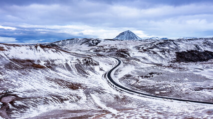Aerial drone view of a road through Hverir geothermal area in Northern Iceland, with Mt. Namafjall in the background. Snow covered winter scene.