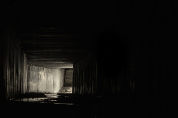 Square dark concrete drainage tunnel with light in the end, with dark free space around.