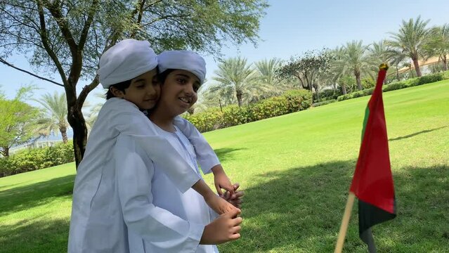 Emirati kids wearing traditional dress kandura playing together in a park. Happy Arab children in white dress from United Arab Emirates