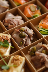 Delicious appetizer snacks delivered in a cardboard box for food catering on a venue. Bruschetta with veal meat and capers prepared for wine party