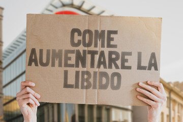 The phrase " How to boost libido " is on a banner in men's hands with blurred background. Desire. Pleasure. Intimate. Intimacy. Relationship. Sex. Private life. Love. Bedroom. Sexual Health