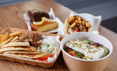 Traditional Greek fast food meal served in recyclable paper dishware. Pita souvlaki meat, fries, white tzatziki sauce and fresh salad prepared for lunch