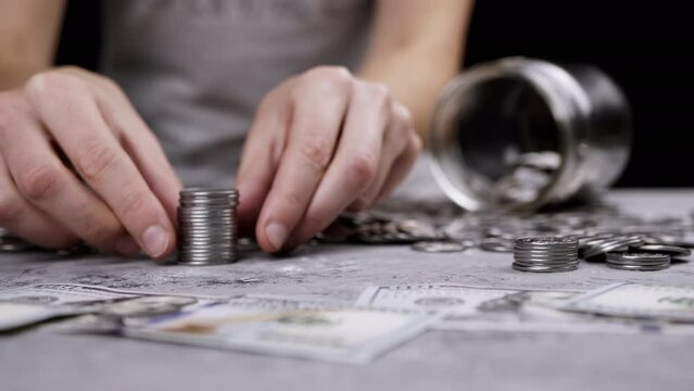 Female Hands Building a Tower from a Stack of Coins near scattered money. Glass jar, piggy bank. Hand places silver cent on top of a tower. Budget, spending, savings, accumulation. Wealth, poverty.