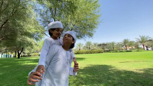 Emirati kids wearing traditional dress kandura playing together in a park. Happy Arab children in white dress from United Arab Emirates