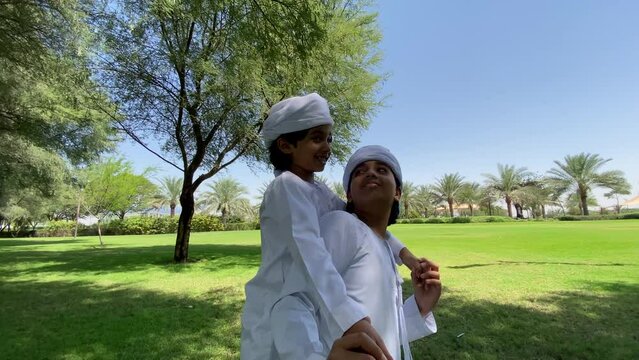 Emirati kids wearing traditional dress kandura playing together in a park. Happy Arab children in white dress from United Arab Emirates