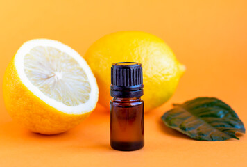 Lemon essential oil. Dark glass bottle with essential oil and lemons on orange background