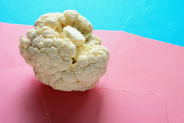 Fresh cauliflower head on blue and pink paper background. Copy space