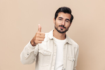 Obraz na płótnie Canvas Portrait of a stylish man smile shows a class sign thumb up on a beige background in a white t-shirt, fashionable clothing style, copy space