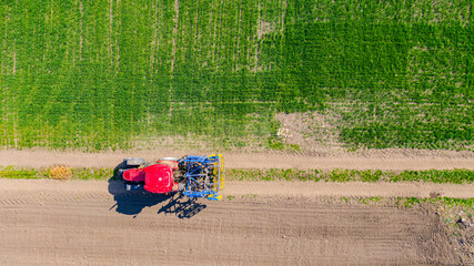 Fototapeta na wymiar Above view, tractor until traveling with seedbed cultivator on dusty road between cultivated fields