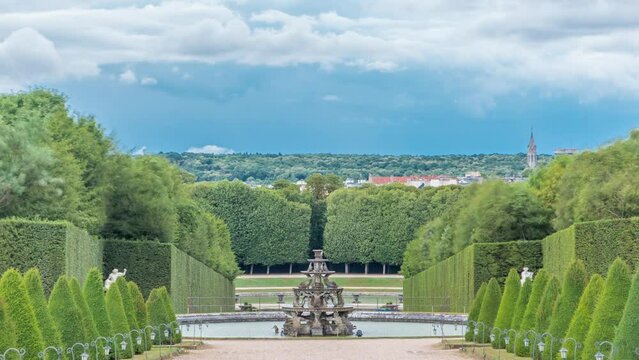 Well-groomed alley in the garden and fountain on background timelapse from above. Beautiful Garden in a Famous Palace of Versailles (Chateau de Versailles), France. Dramatic cloudy sky at summer day