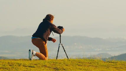 Photographer on the hill. Young male photographer takes pictures with camera and telephoto lens set...