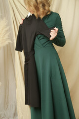 Young woman in fashion atelier choosing between green and black dress