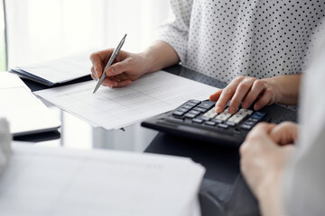 Woman accountant using a calculator and laptop computer while counting taxes for a client. Business audit and finance concepts