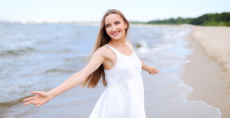 Happy smiling woman in free happiness bliss on ocean beach standing with open hands. Portrait of a multicultural female model in white summer dress enjoying nature during travel holidays vacation
