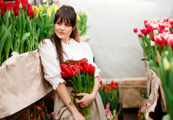 A model among tulips at a spring photo shoot. Modern clothes of a farmer. Ukrainian girls are very beautiful. Long hair