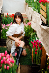 A model among tulips at a spring photo shoot. Modern clothes of a farmer. Ukrainian girls are very beautiful. Long hair