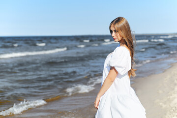 Fototapeta na wymiar Happy, beautiful woman on the ocean beach standing in a white summer dress. Portrait
