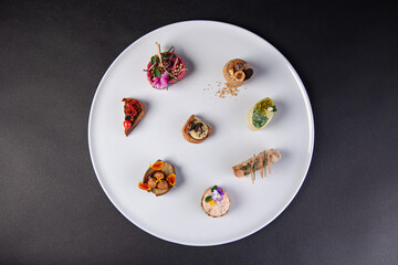 top view on various gastronomic appetizer on a white plate isolated on a black background