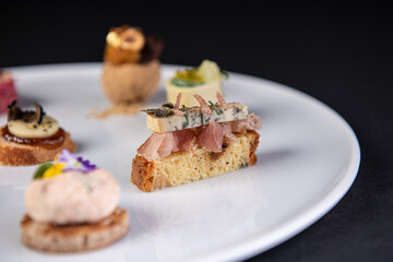 focus on various gastronomic appetizer on a white plate and black background,culinary arts