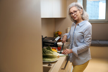 Pleasant elderly woman in kitchen home is engaged in cooking