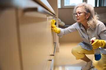 Cute slender grandmother washes kitchen surfaces squatting