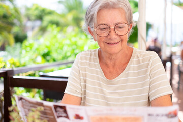 Carefree attractive smiling senior woman sitting in outdoor cafe table looking and choosing food...