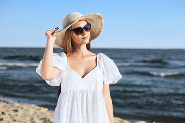 Fototapeta na wymiar Happy blonde woman is posing on the ocean beach with sunglasses and a hat. Evening sun