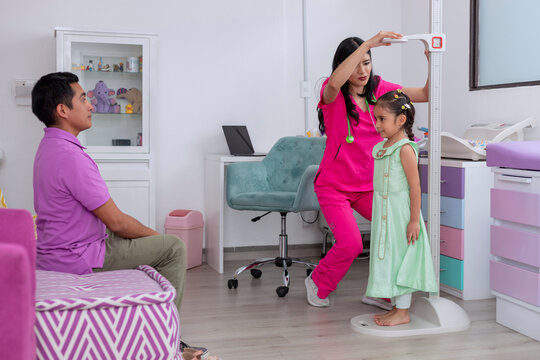 Dad with his daughter in the pediatrician doctor's office, while they measure the girl's height with a pedestal ruler