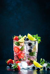 Strawberry and blueberry mojito cocktail drink with lime, white rum, soda, cane sugar, mint, and...