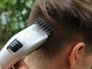 cutting the dark hair of a young man with an electric trimmer, a close-up of a male nape from which...