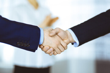 Business people shaking hands at meeting or negotiation, close-up. Group of unknown businessmen and a woman standing in a modern office. Teamwork, partnership and handshake concept