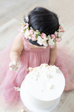 one year old baby girl in a pink flower crown with a white cake smash and a pink tulle dress